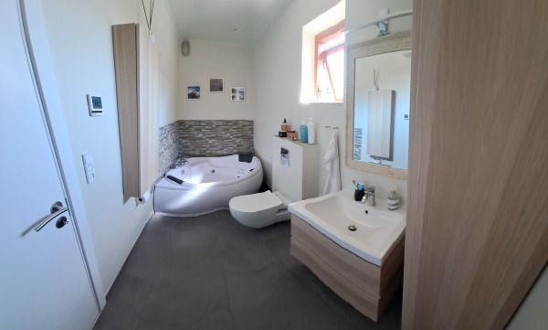 Moderne badeværelse med badekar, toilet og håndvask i trælook, samt lys indretning og store vinduer.
