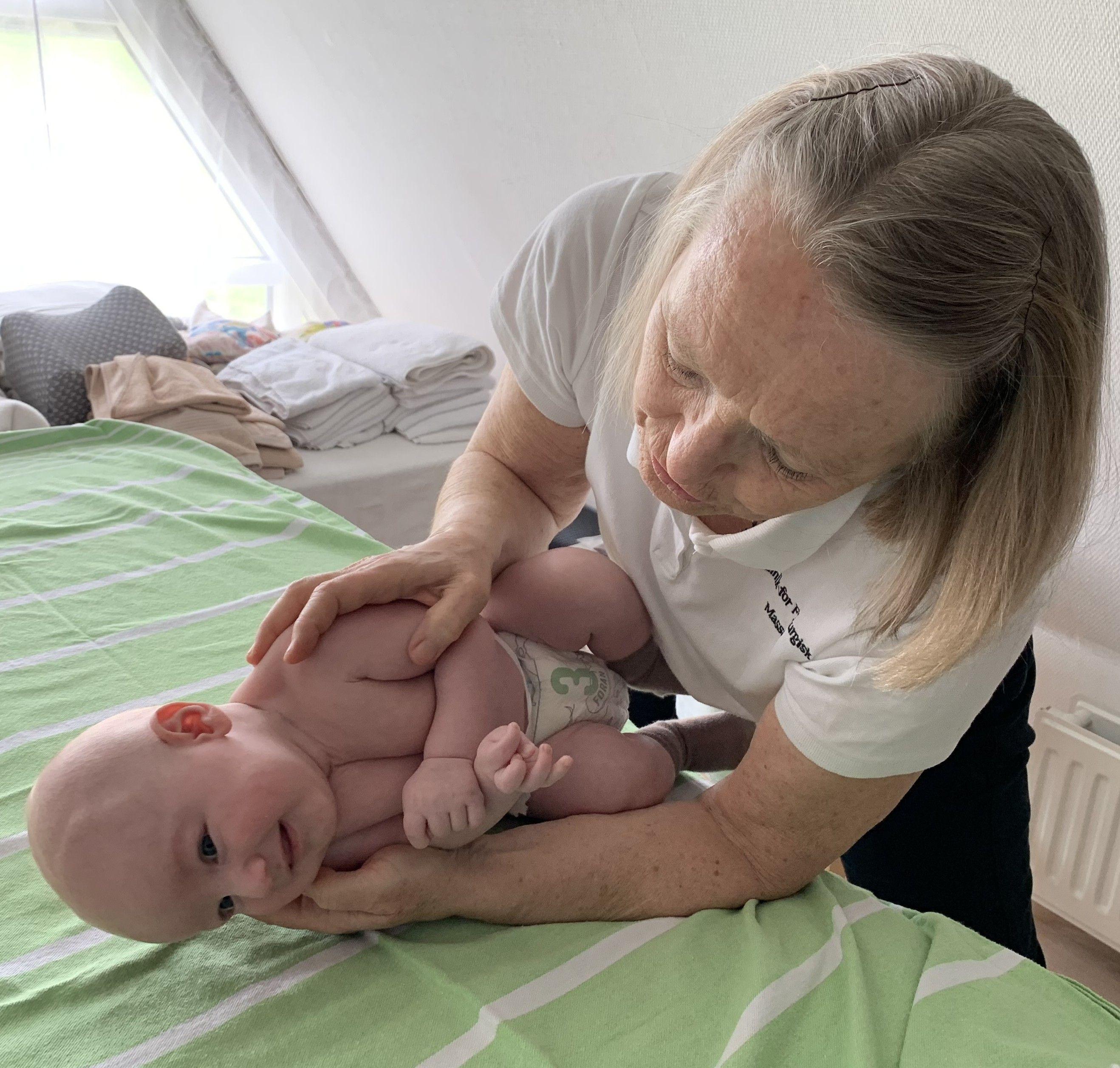 En ældre kvinde holder en baby på en seng med grønne lagner, mens de begge ser op.