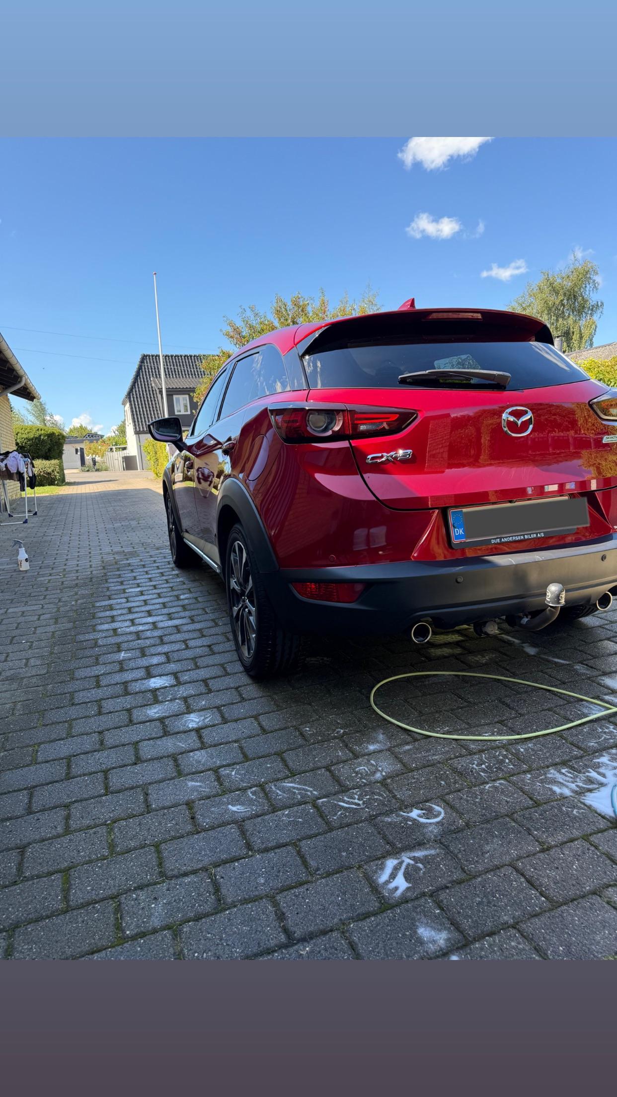 Rød SUV parkeret på en brostensbelagt indkørsel med blå himmel og skyer i baggrunden.