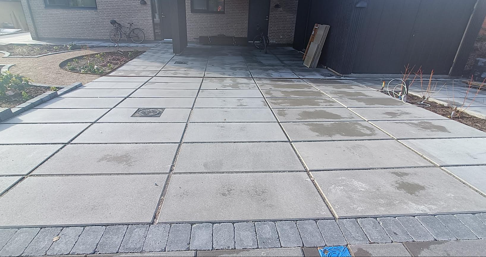 Nybelagt betonindkørsel med fliser og gruskanter i en moderne bolig.