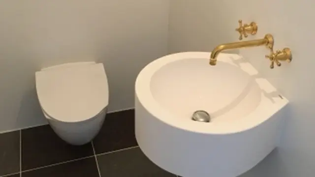 Moderne badeværelse med hvidt toilet og en rund vask med gyldne haner.