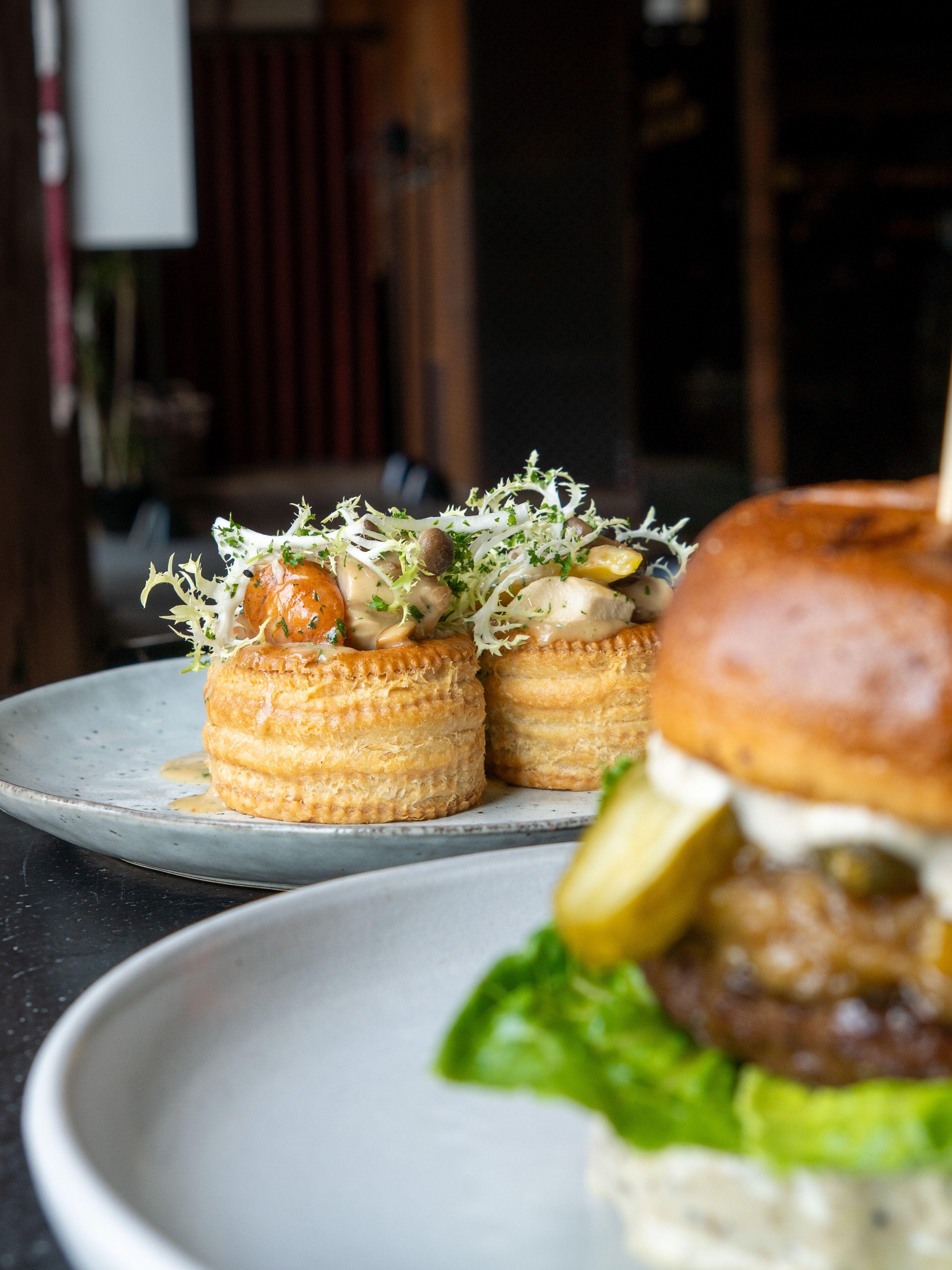 Saftig burger med salat og pickles, serveret med sprøde tærter fyldt med grøntsager.
