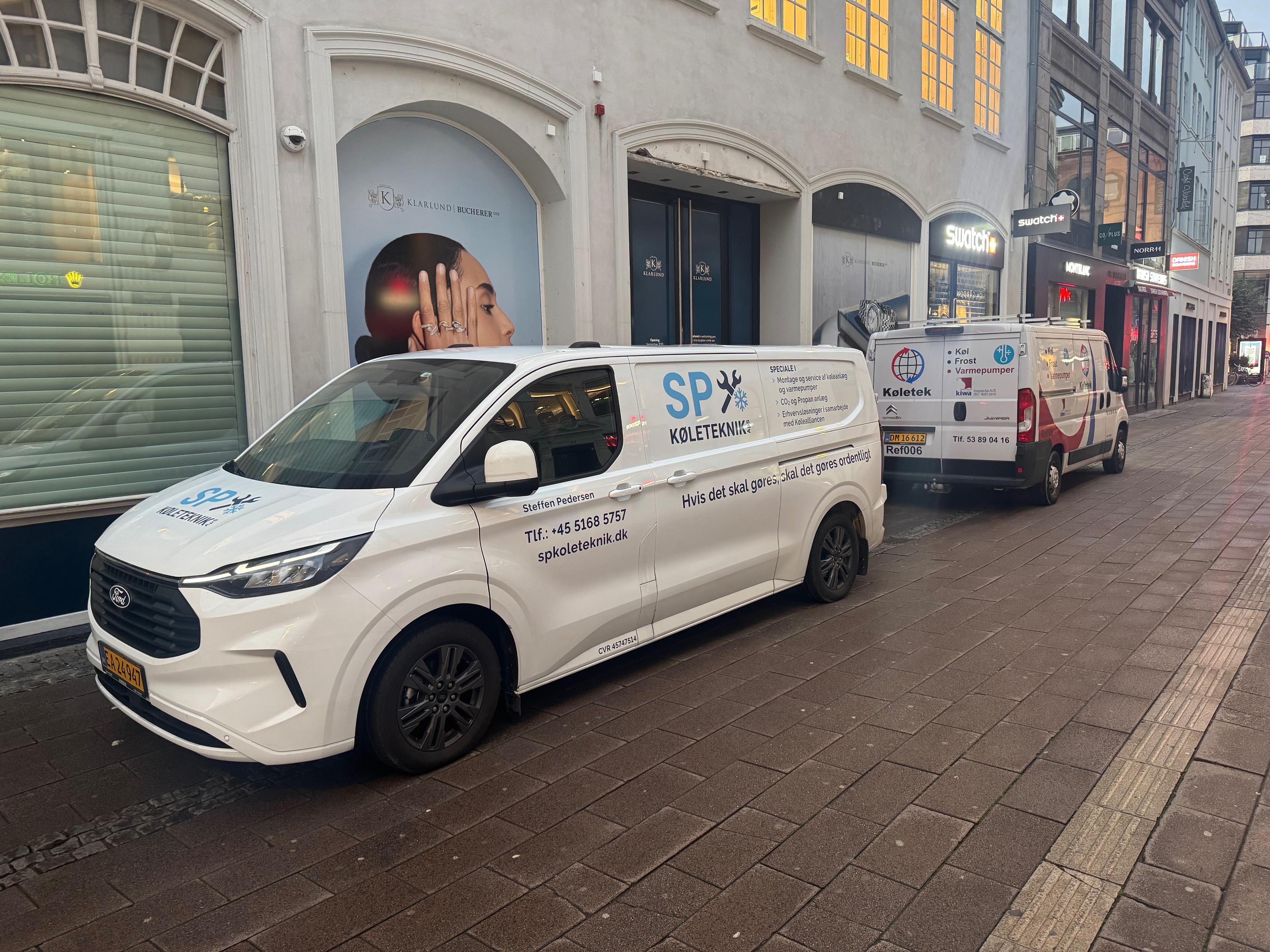 To biler parkeret på en gade, begge med logoer fra SP, en servicevirksomhed.