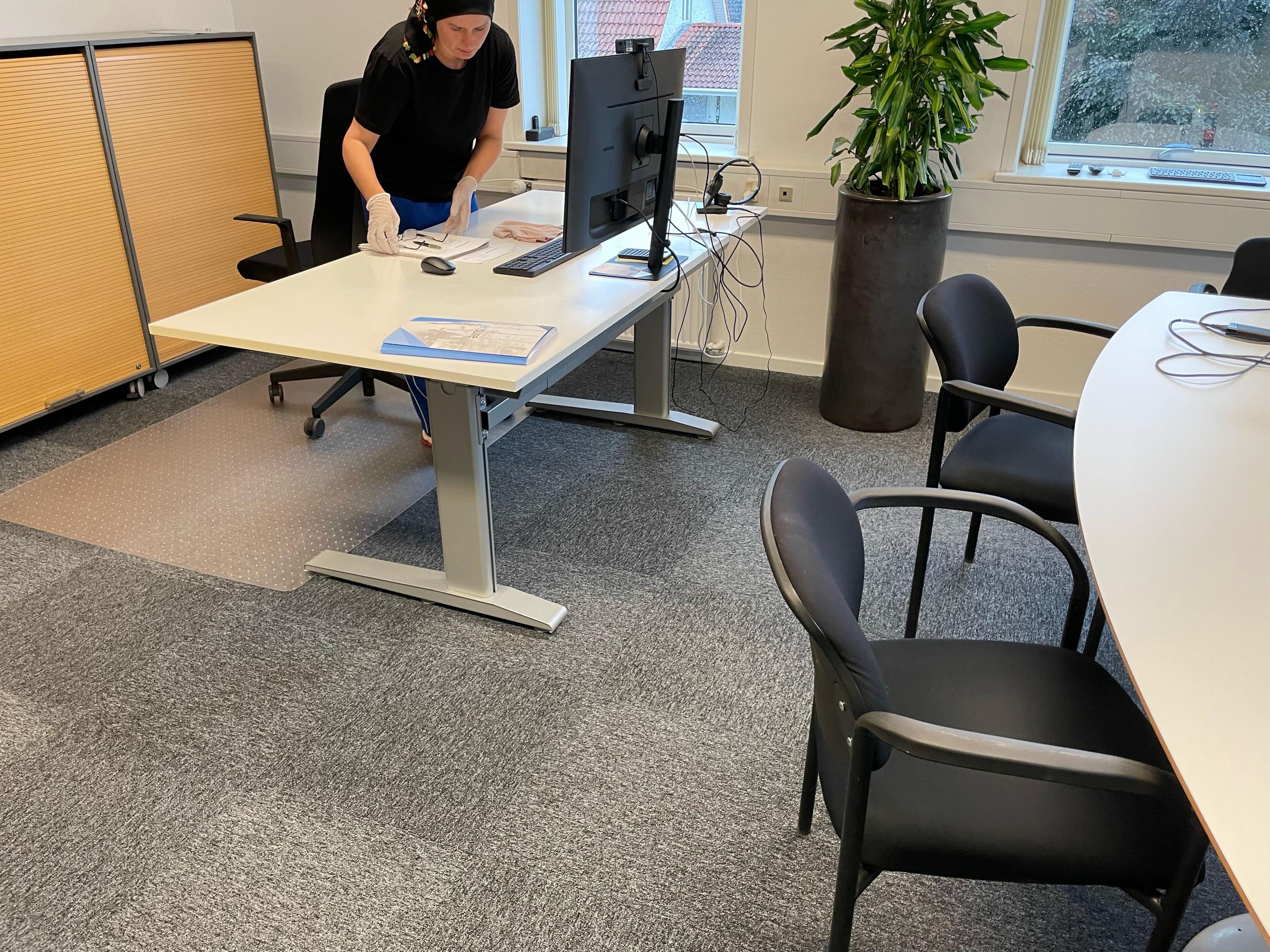 En person arbejder ved et skrivebord i et moderne kontor med en computer og planter i baggrunden.