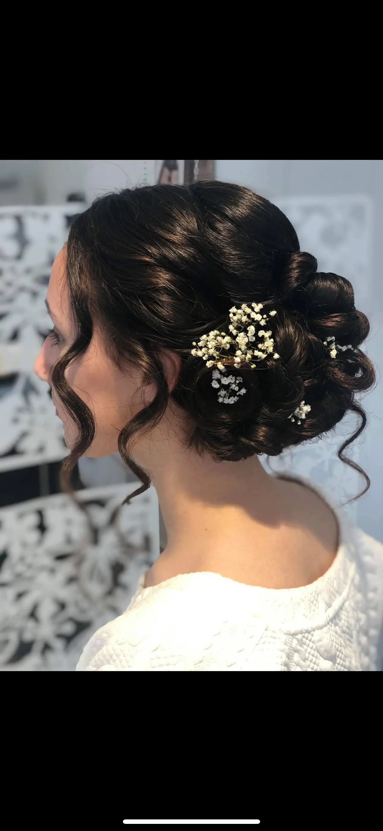 En kvinde med en elegant opsætning af hår dekoreret med små blomster, set fra siden.
