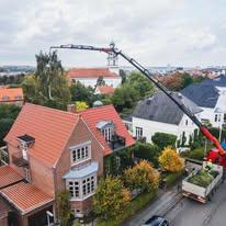 En kran fjerner grene fra et hus i en by med farverige bygninger og træer i efterårsfarver.