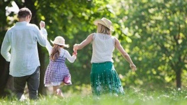 Familie går hånd i hånd i en grøn park, mens de nyder en solrig dag. Børn i hat og farverige tøj.
