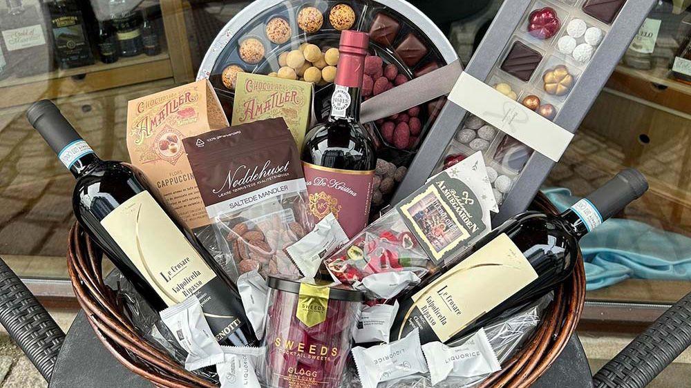 En kurv med rødvin, chokolade, og snacks, perfekt til en gave eller fest.