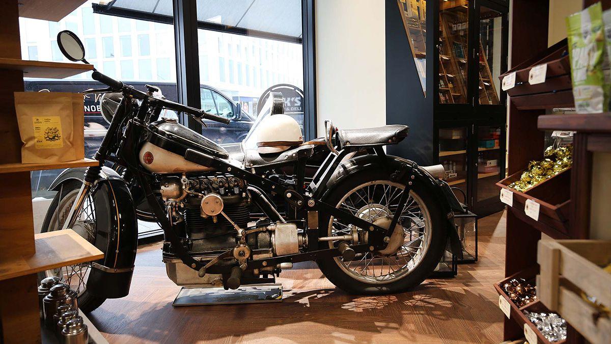 En klassisk motorcykel i en butik med træhylder og vinduer, der viser en moderne by.