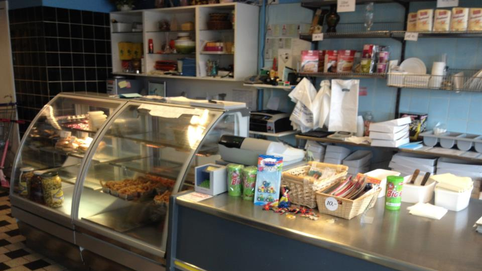 Bageri med glasvitrine, kager, brød og kasseapparat på disken i en hyggelig butik.
