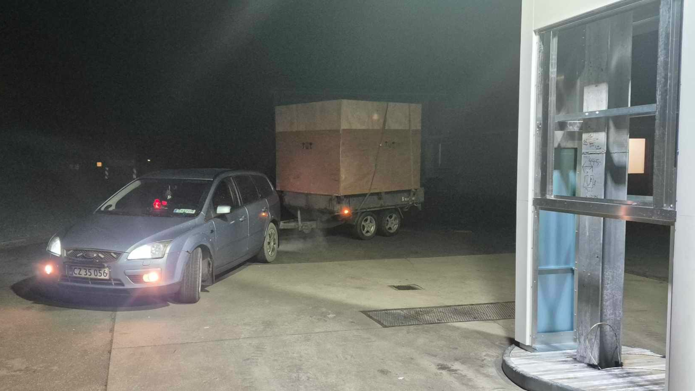 En bil med en trailer, der trækker en stor kasse, parkeret ved en bygning om natten.