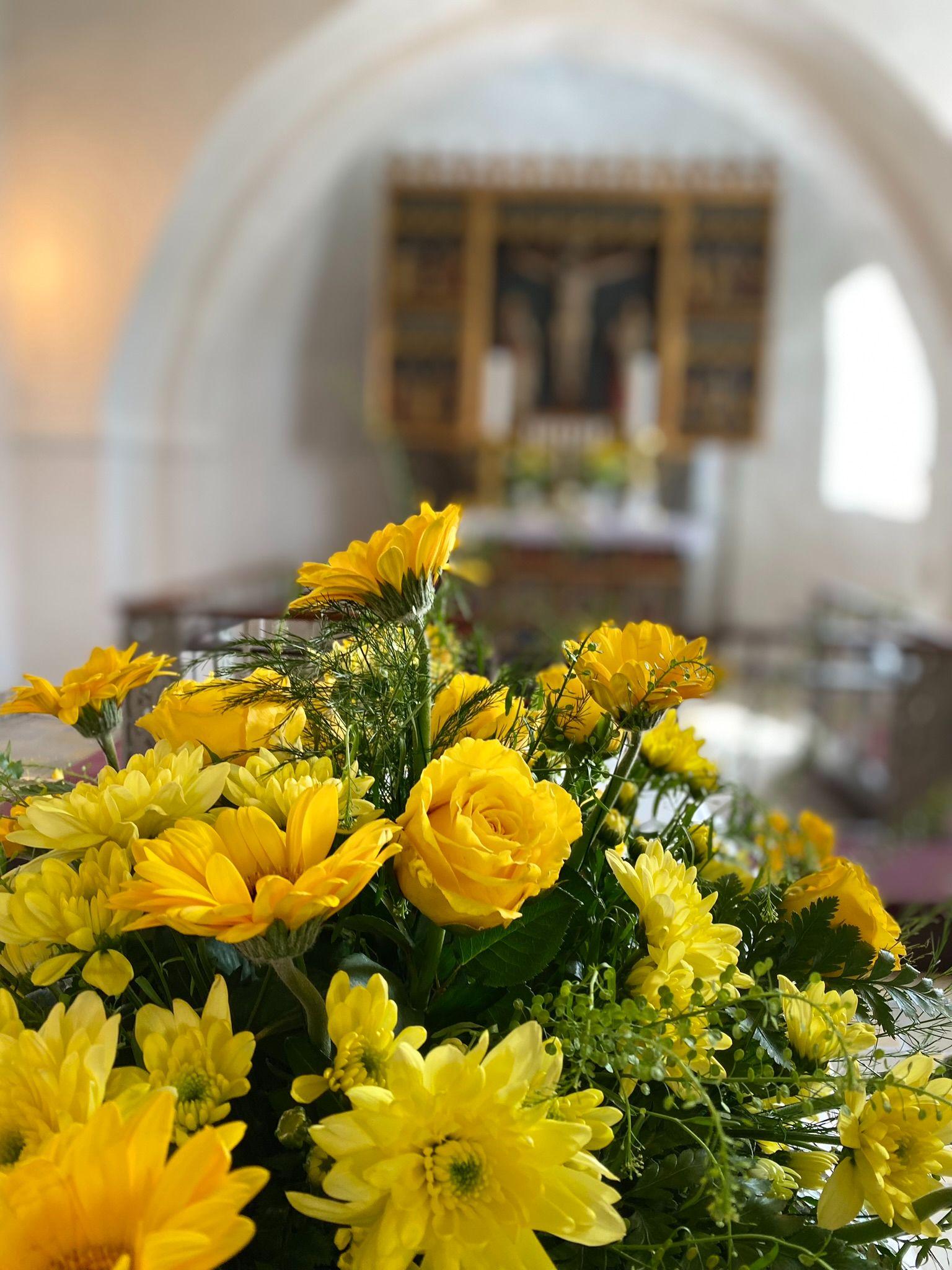 En farverig buket med gule blomster i forgrunden, med en kirkeindretning i baggrunden.
