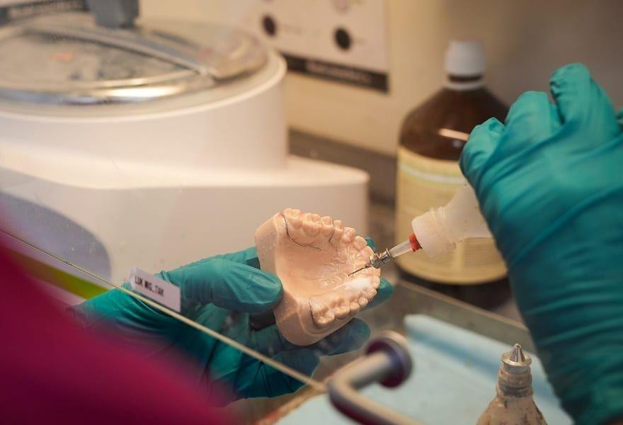 En tandlæge arbejder med en tandmodel og påfører væske med en pipette i et laboratorium.