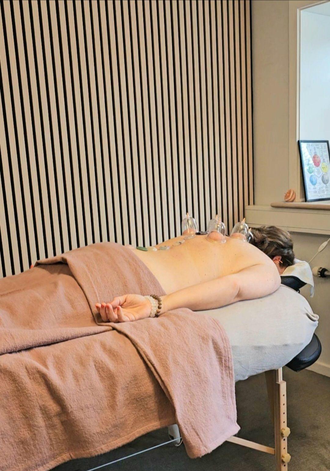 En person ligger på en massagebriks med håndklæder, mens de får behandling i et lyst rum.