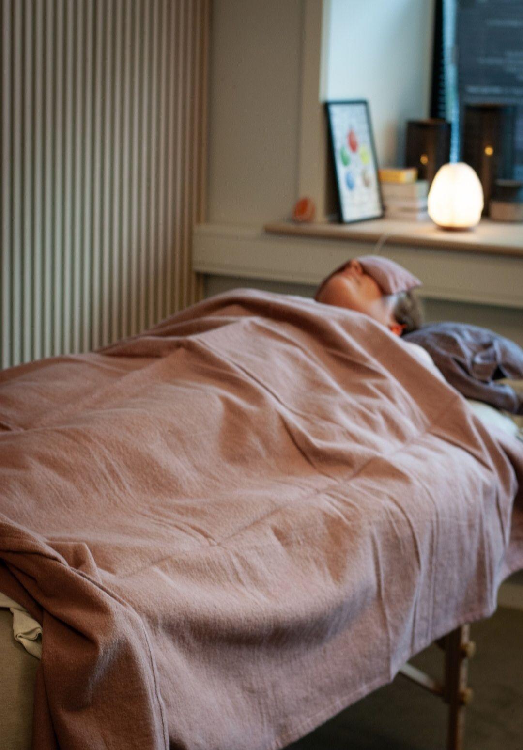 En person ligger afslappet under en lyserød dyne på en massagebriks i et lyst rum.