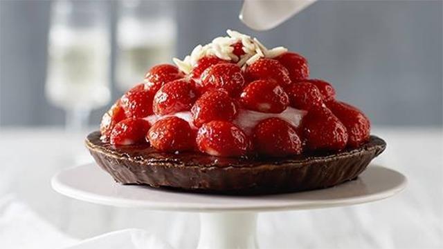 En lækker chokolade tærte toppet med friske jordbær og flødeskum, serveret på en hvid kagefad.