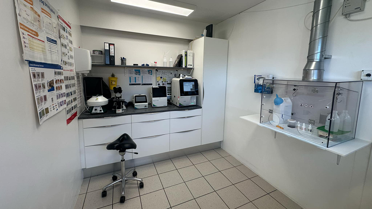 Laboratorium med hvide skabe, udstyr til forskning og en arbejdsstation med stole og forskellige apparater.