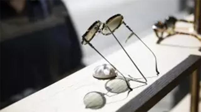 Sorte solbriller med metalstel ligger på en hylde ved vinduet i en butik.