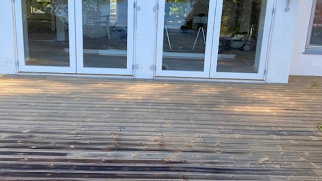 Terrasse med træplanker foran glasdøre, der fører ind til et lyst rum.