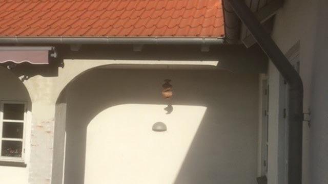 En væg med en lampe og skygger fra taget på et hus med rød tagsten.