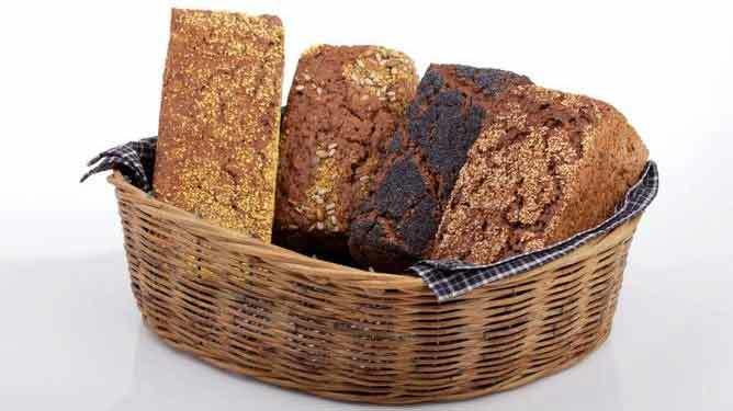 En kurv med forskellige brødtyper, herunder rugbrød og groft brød, præsenteret på en hvid baggrund.