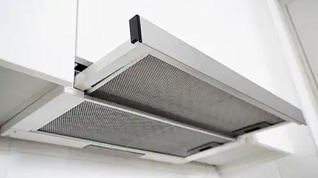 Køkkenventilator med metalfilter monteret under et skab i et moderne køkken.