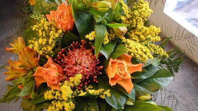 En farverig buket med orange roser, gule blomster og grønne blade.