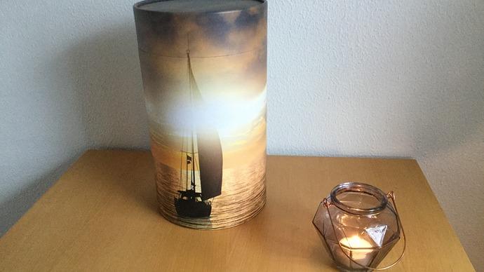 En lampe med et sejlskib i solnedgang og en glaslysestage på et træbord.