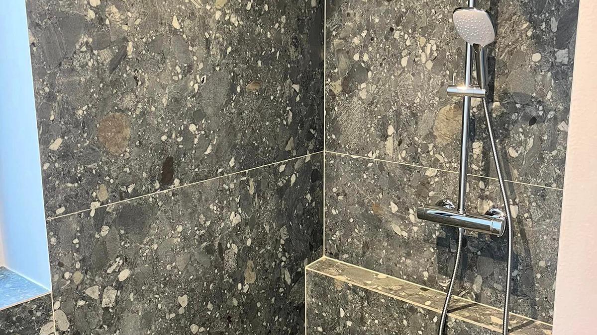 Moderne bruser med grå marmorvægge og kromarmatur i et stilrent badeværelse.