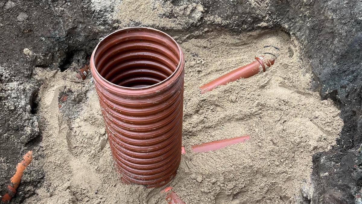 Rør i en gravet grøft, omgivet af sand og med synlige røde markeringer på jorden.