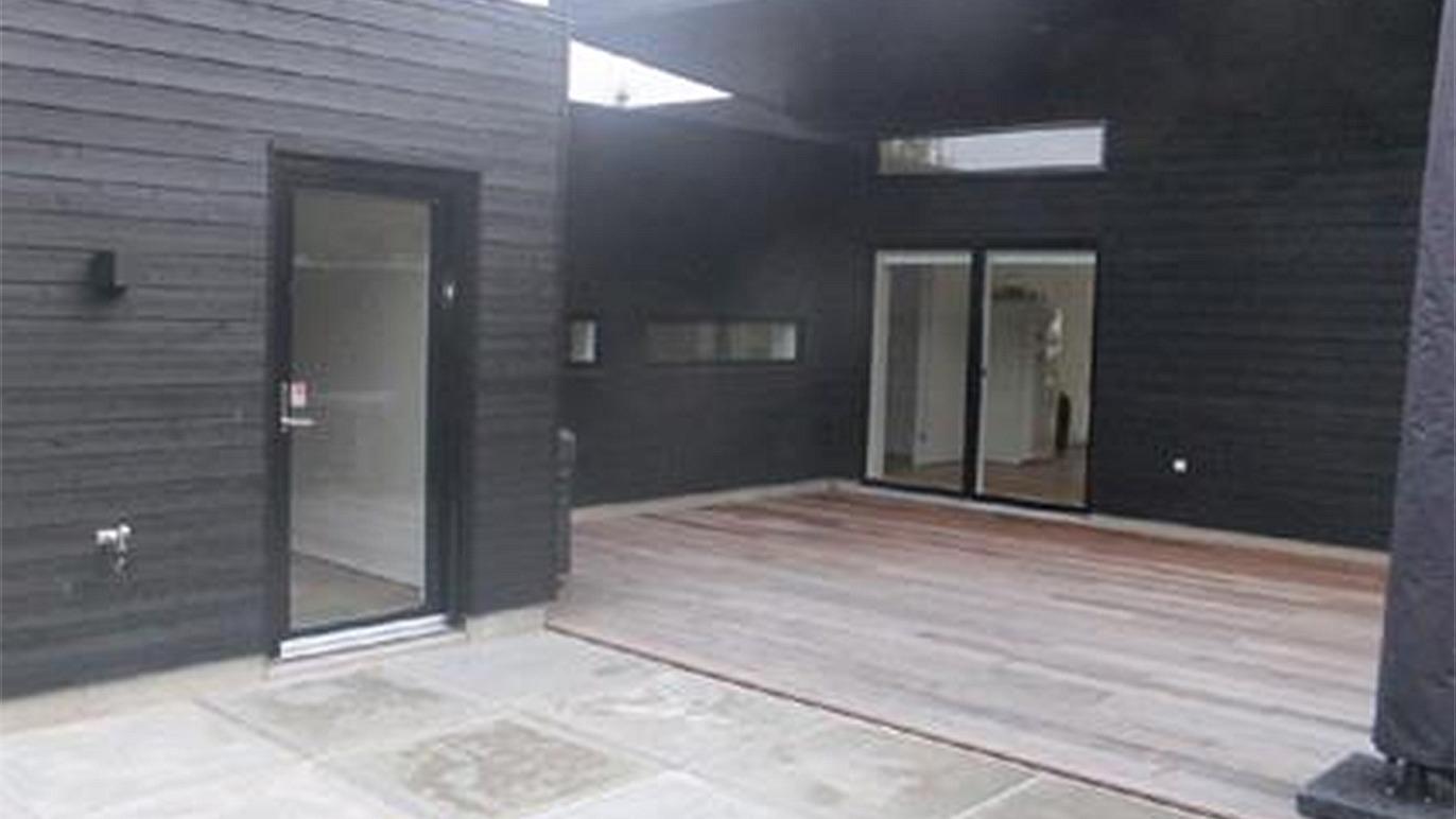 Moderne sort hus med en åben terrasse og store vinduer, der giver masser af lys indendørs.