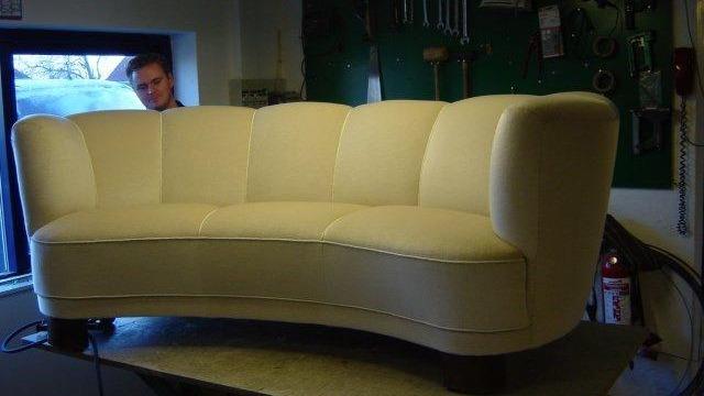 En lys beige sofa med buet ryg og træben står på et bord i et værksted.