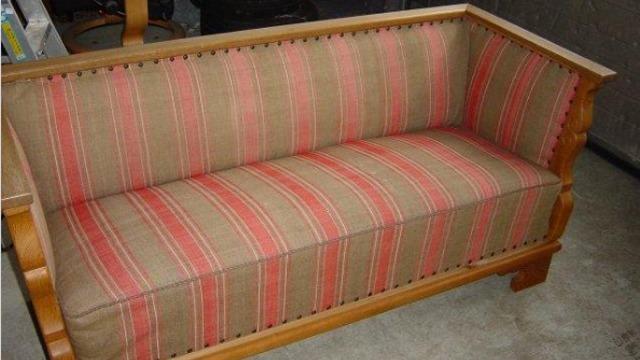 En klassisk sofa med stribet betræk i brune og røde nuancer, placeret på et gråt gulv.