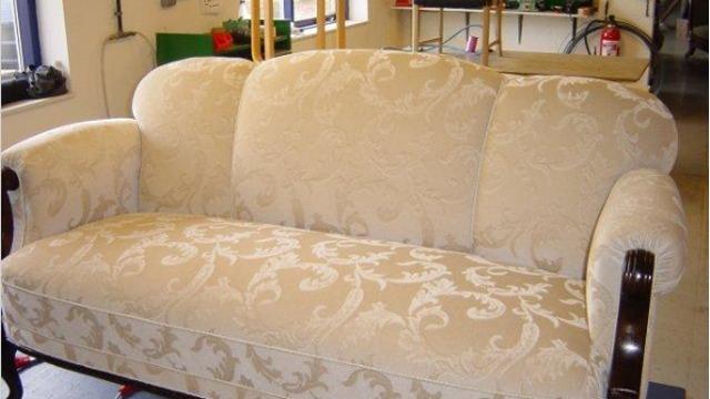 En beige sofa med mønster og træben, placeret i et lyst rum med indretning i baggrunden.