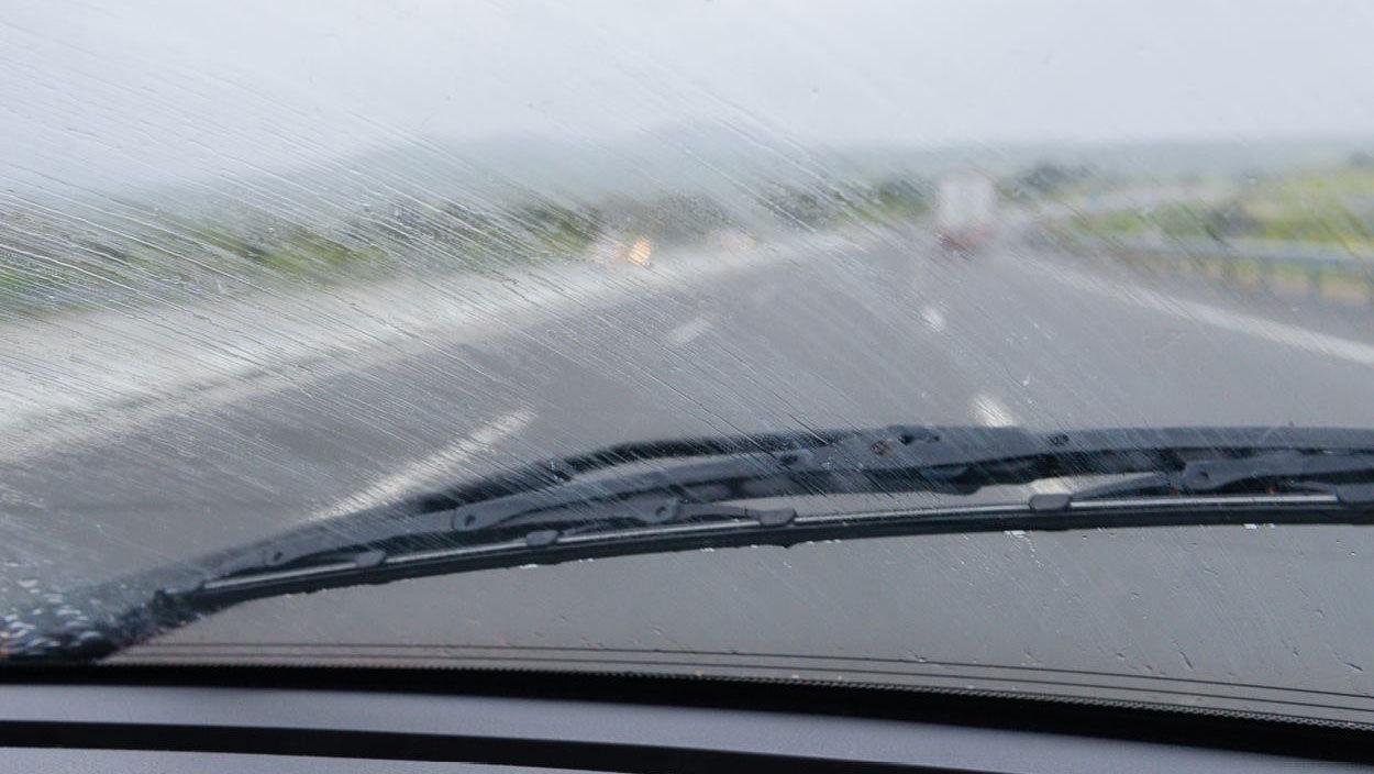 Udsigt fra en bil med våde forrude, der viser en regnvejrsvej på motorvejen.