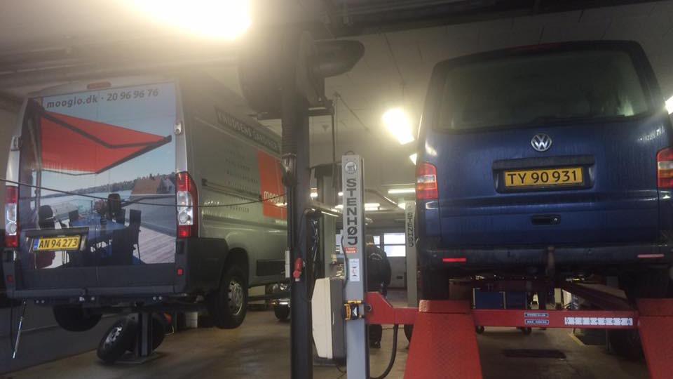 To biler på værksted, en varevogn og en personbil, begge hævet på lift til reparation.