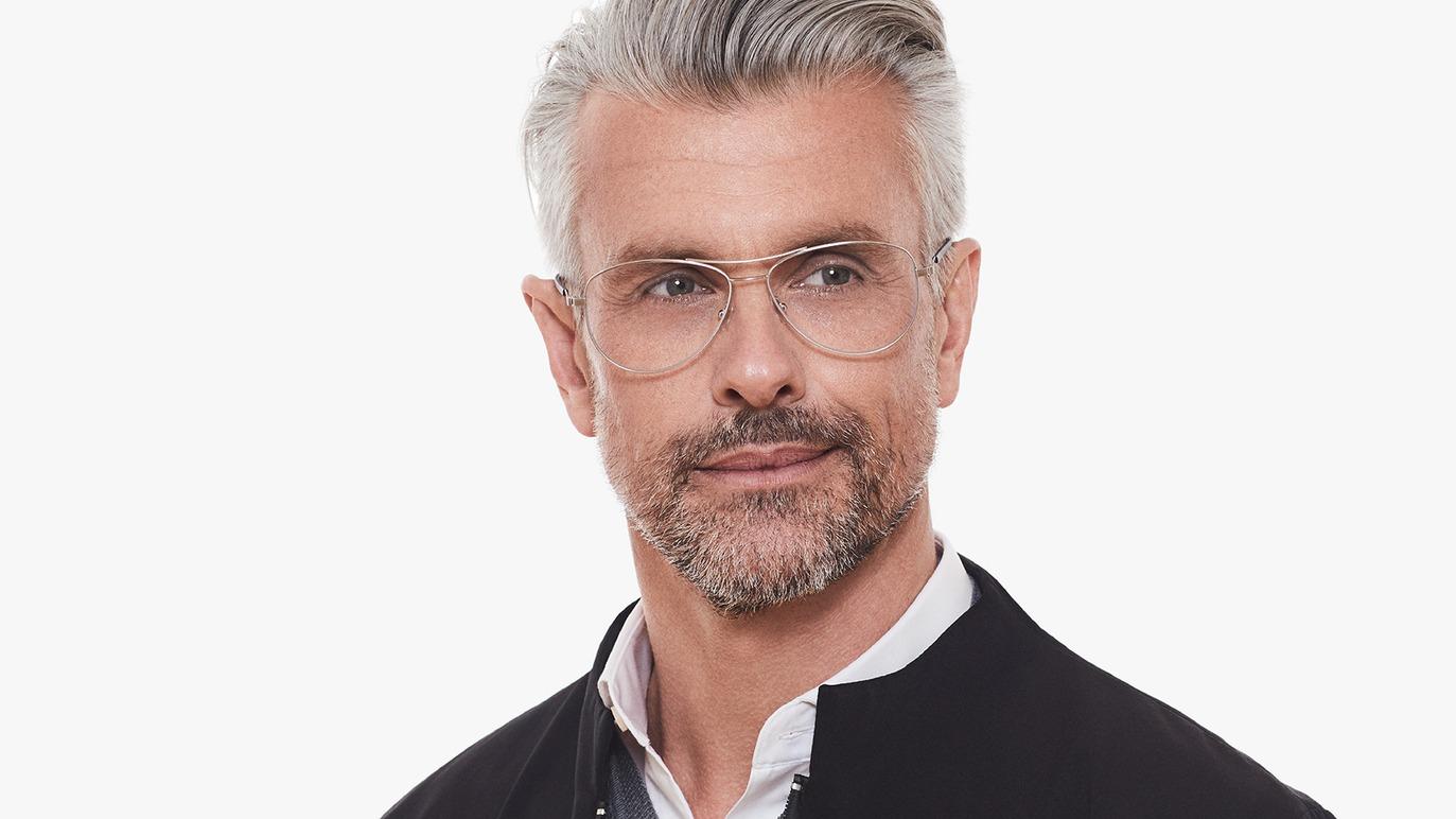Mand med gråt hår og briller, iført sort jakke, smiler let mod kameraet.