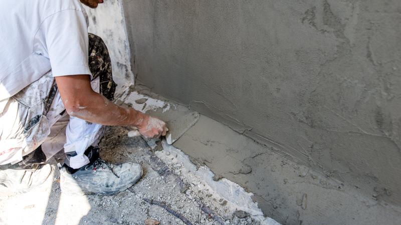 En håndværker påfører cement på en væg med en spartel i et byggeprojekt.