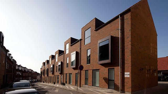 Moderne murstensbygninger med store vinduer i en bygade under en klar himmel.