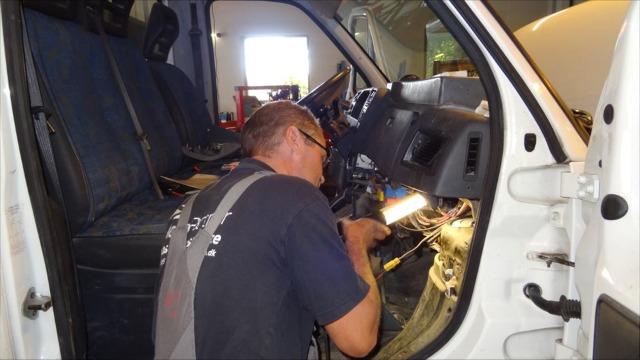 En mekaniker arbejder på bilens instrumentbræt i en garage med værktøj og ledninger.