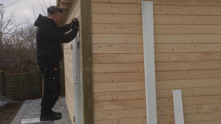 En mand står på en platform og arbejder på væggen af et træhus.