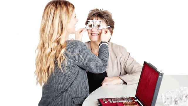 En optiker justerer briller på en smilende kvinde ved et bord med et brilleværktøjssæt.