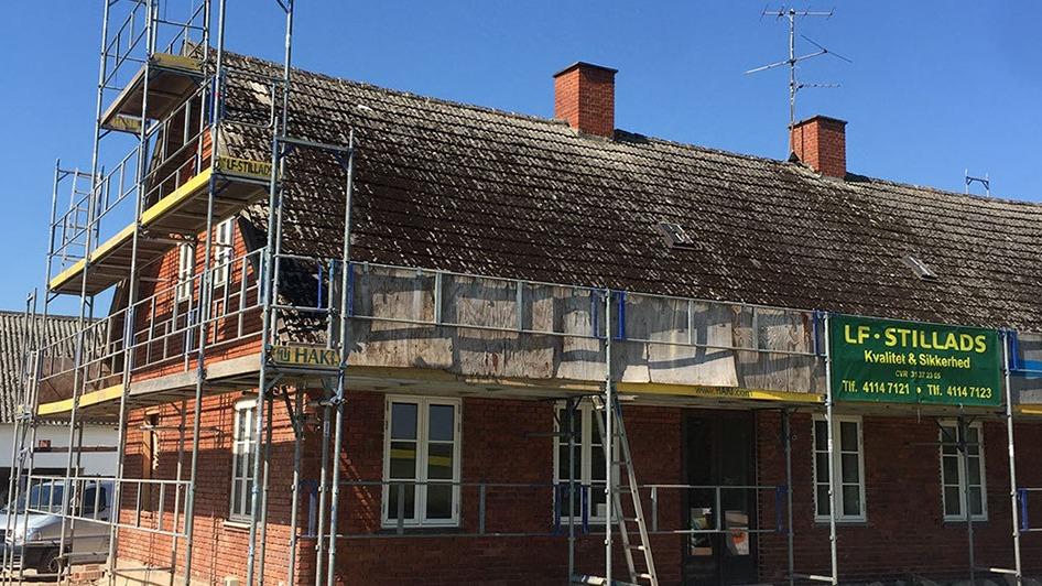 Hus under renovering med stillads og tagarbejde, beliggende i solrigt vejr.