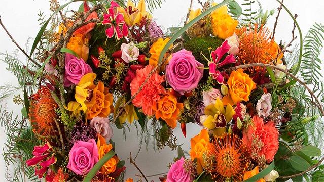 En farverig blomsterkrans med roser, orkideer og forskellige blomster i nuancer af pink, orange og gult.