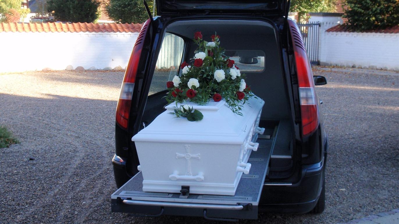Kiste med blomsterarrangement i bagagerummet på en bil, klar til transport til begravelse.