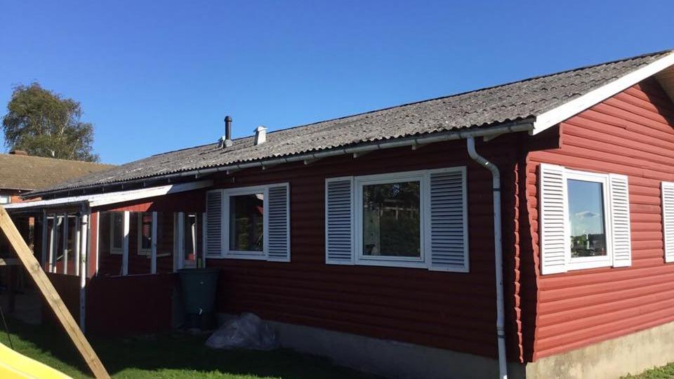 Rødt hus med hvide vinduer og tag, beliggende under en klar blå himmel.