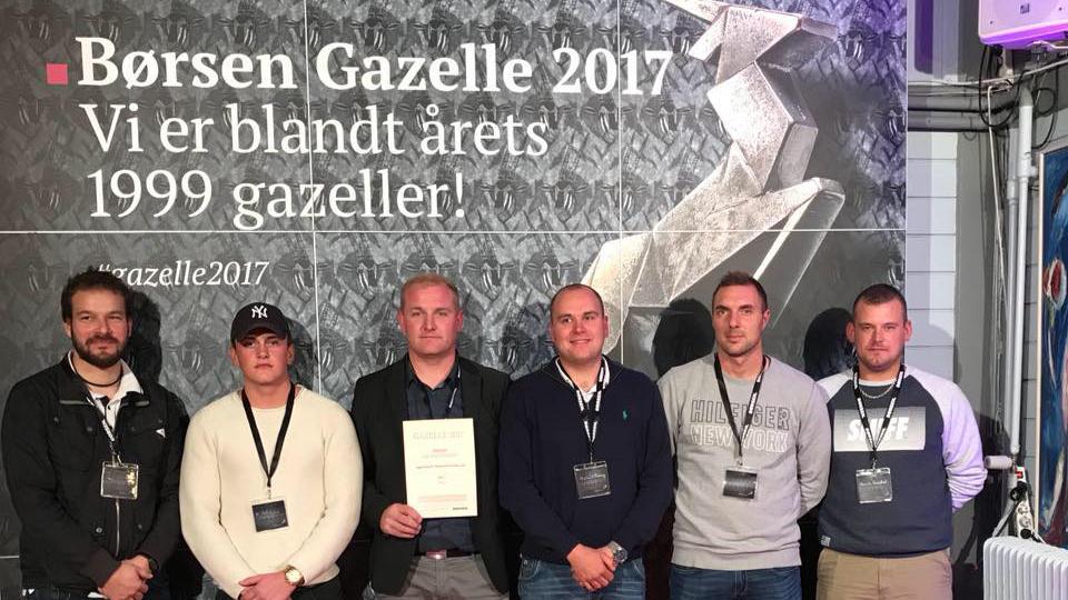 Gruppe af mænd står foran en væg med teksten "Børsen Gazelle 2017" og holder et certifikat.