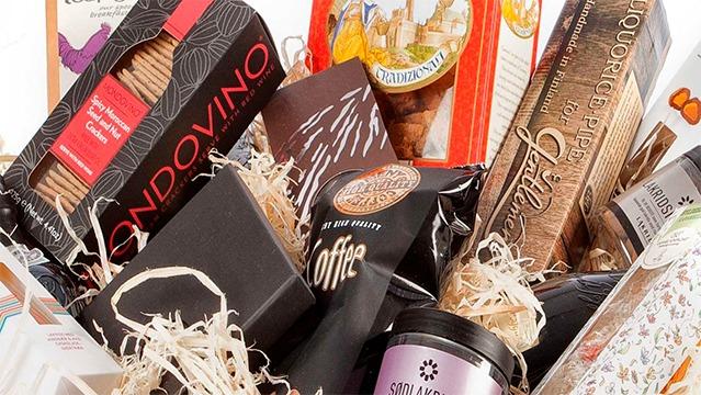 Gavekurv fyldt med lækkerier som småkager, chokolade, vin og gourmetprodukter.