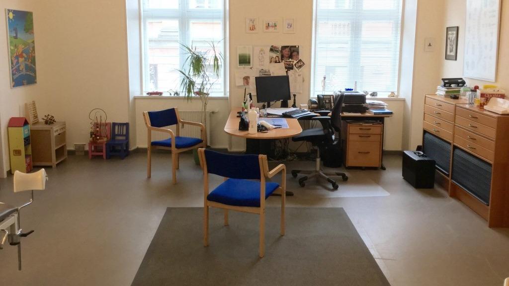 Et kontor med to blå stole, et skrivebord, en computer og opbevaringsskabe ved vinduerne.