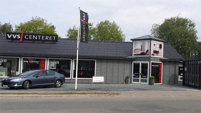VVS Centeret med en grå bil parkeret foran og en stor reklame på bygningens facade.